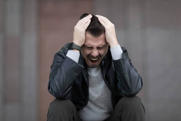 a man with a migraine attack sits clutching his head and screaming a man with a migraine attack sits clutching his head and screaming. terrified stock pictures, royalty-free photos & images