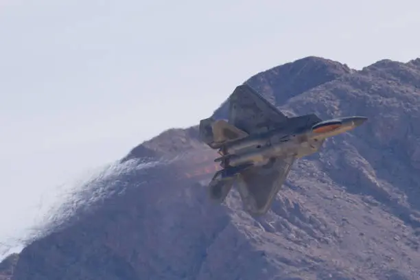 F-22 Raptor in a tight turn against the Nevada hills, with afterburners on and  the jet stream visible behind the aircraft