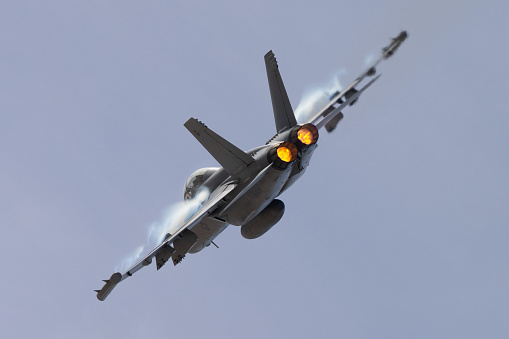 Very close tail view of a U.S. Navy EA-18G Growler in a high G maneuver, with afterburners on and condensation clouds  at the wings