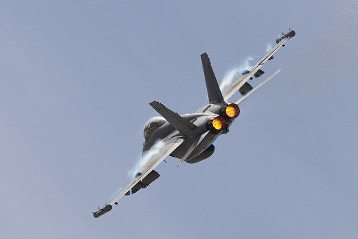 Very close tail view of a U.S. Navy EA-18G Growler in a high G maneuver, with afterburners on and condensation clouds  at the wings