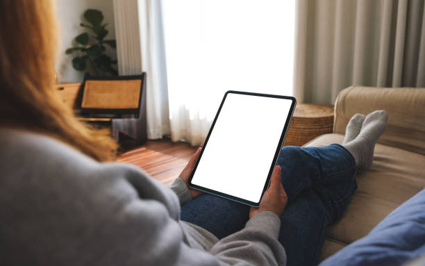 istock Mockup image of a woman holding digital tablet with blank desktop screen while lying on a sofa at home 1455633408