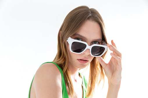 Blonde freckled girl wearing sunglasses. Photo studio with sunlight.