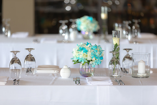 dinner table In the wedding ceremony set up with a bouquet of orchids White and blue and rose, with wine glasses, rehearsal spoons, napkins, beautiful bokeh. in a hotel