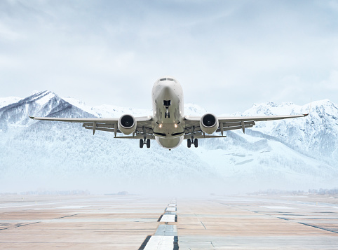 White passenger aircraft take off from airport runway against the backdrop of picturesque snow capped mountains