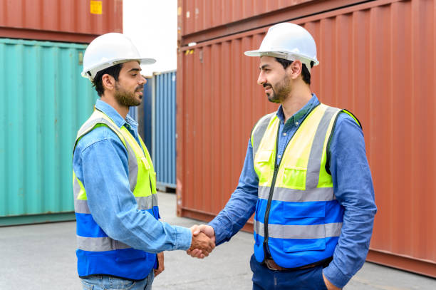 istock Two engineer container cargo wearing white hardhat and safety vests in successful handshake together at container yard. success in logistics business import export industry 1455647492
