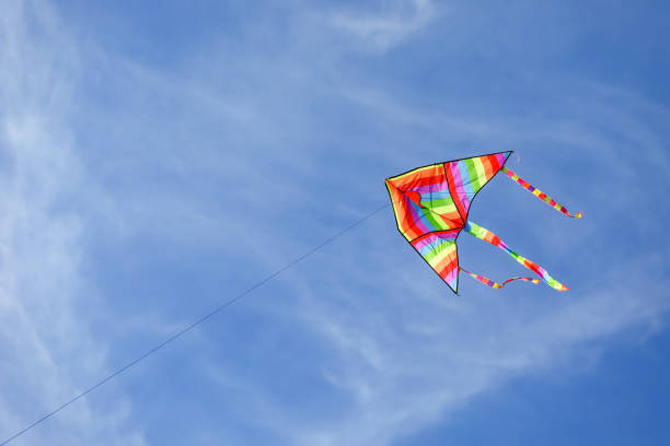istock rainbow colored kite flying high in the blue sky with some white clouds 1455650166