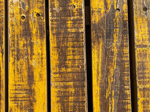 Stock photo showing close-up view of weathered and worn hardwood timber fencing. The aged yellow painted wood planks shows dirty wood grain caused by weather conditions.