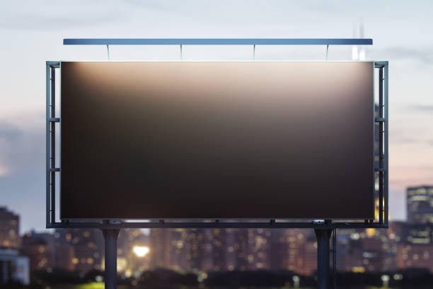 istock Blank black billboard on cityscape background at evening, front view. Mock up, advertising concept 1455657829