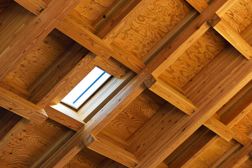 Low angle view of a wooden roof structure with beams with skylight.