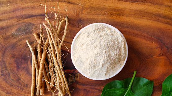 Ashwagandha Roots and powder known as Withania somnifera in white bowl on wooden background. Indian ginseng, poison gooseberry, or winter cherry. Herbal adaptogen ayurvedic medicine.