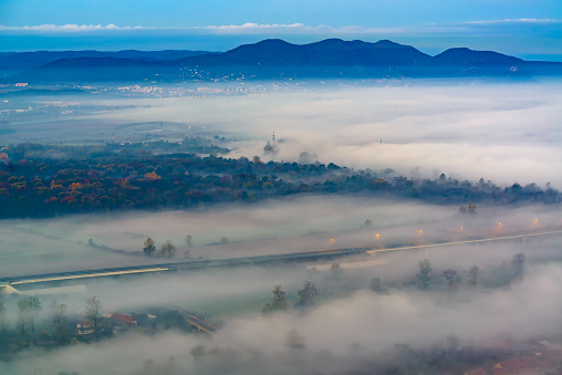 Aerial view of the town in the early morning mist is beautiful in the highlands. Low clouds and fog cover the sleeping city, photo in full moon light. Alpine mountain valley mists landscape at dawn