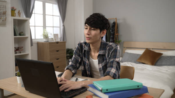 felice studente coreano maschio asiatico che impara da casa sul laptop in camera da letto - contemporary domestic room sparse indoors foto e immagini stock