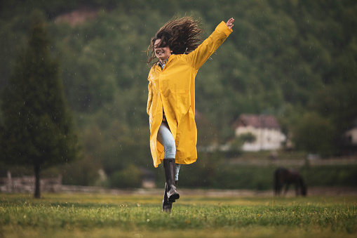 Young carefree woman in raincoat having fun during rainy day with her arms outstretched. Copy space.