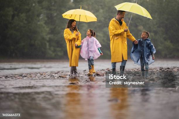 Carefree Family In Raincoats Walking By The River On A Rainy Day Stock Photo - Download Image Now