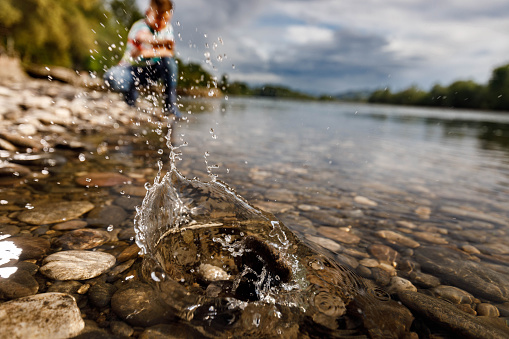 Close up of a stone splashing into water while little boy is in the background. Copy space.