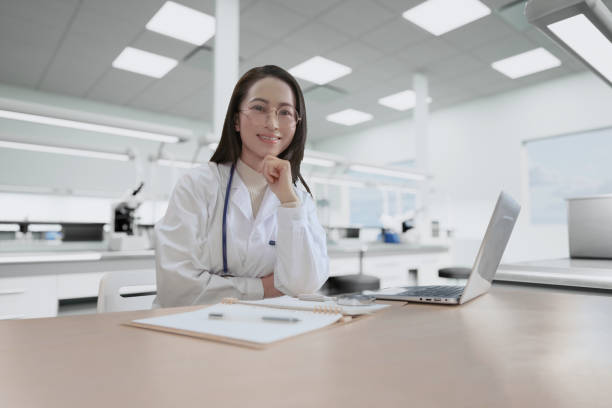 doctor sitting at desk and writing a prescription for her patient - japanese ethnicity women asian and indian ethnicities smiling imagens e fotografias de stock