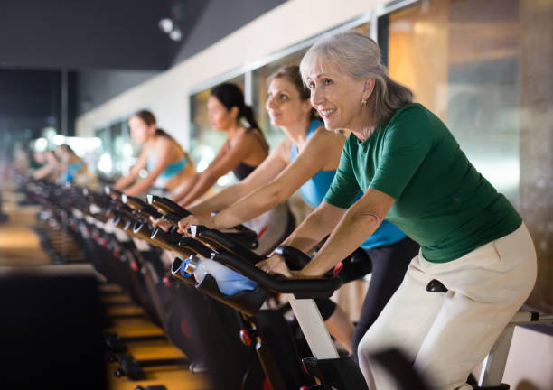 зрелая женщина, посещающая занятия велоспортом в тренажерном зале - exercising sport gym spinning стоковые фото и изображения