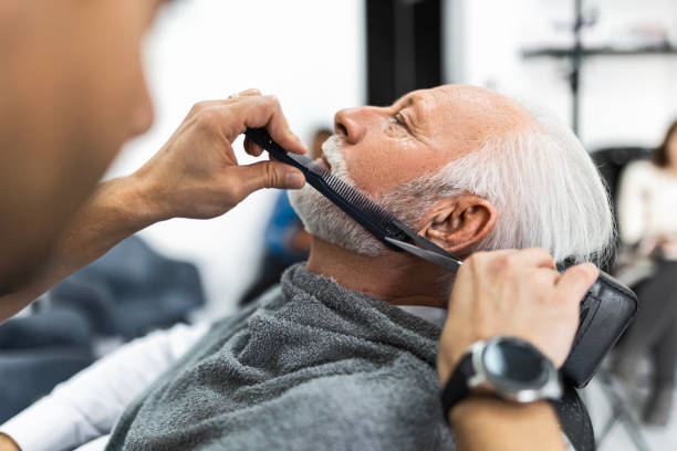 istock Senior man at barber getting his beard trimmed with use of comb and scissors 1455669589