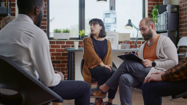 istock Woman with nervous behavior sharing mental health issues with people at a group therapy session 1455671896