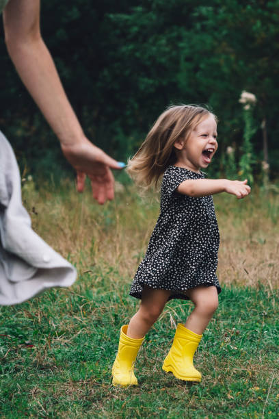 maman et fille jouent au rattrapage ou au bêtisier dans la nature dans un parc ou un village. jeux actifs avec un enfant au grand air. le concept d’une enfance heureuse. la fille court joyeusement la bouche ouverte - family mouth open vertical mother photos et images de collection