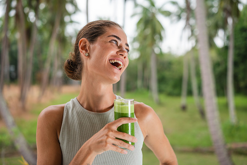 Portrait of a smiling, young woman holding a glass of healthy, green smoothie.