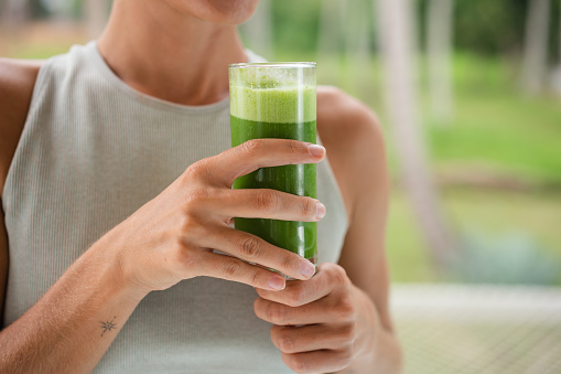 Midsection of an unrecognizable woman holding a glass of healthy, green smoothie.
