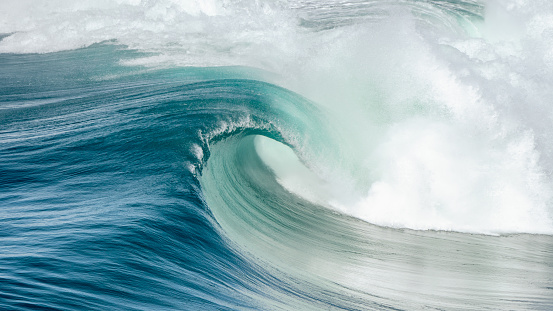 Cresting teal blue wave breaking in open ocean