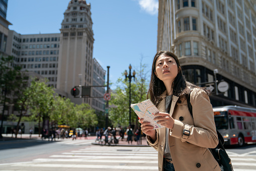 lost asian korean female tourist looking into distance while using city map on street corner near triangular phelan building in financial district of san Francisco in California usa.