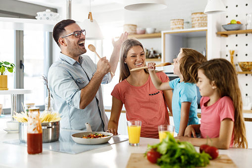 Happy parents and their small kids having fun while preparing a meal together in the kitchen.