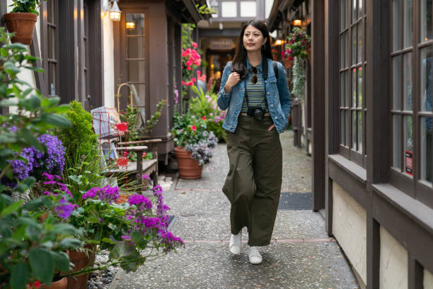 full length of leisure asian Japanese woman visitor walking through beautiful passageway with flower pots between restaurants during her visit in Carmel by the sea full length of leisure asian Japanese woman visitor walking through beautiful passageway with flower pots between restaurants during her visit in Carmel by the sea city of monterey california stock pictures, royalty-free photos & images