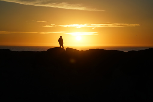 A silhouette of a man standing on a hill during the sunset
