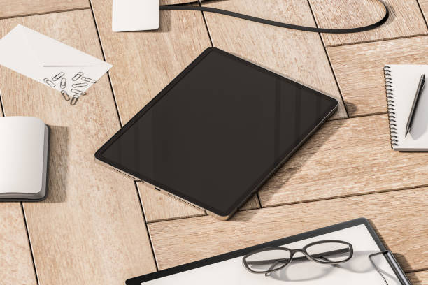 istock Perspective view on blank dark modern digital tablet screen with space for your logo or text on wooden surface background with office tools and glasses. 3D rendering, mock up 1455678776