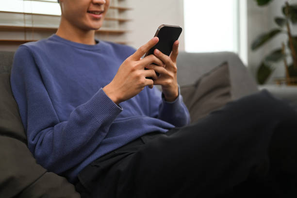 istock Cropped shot of man typing text message, chatting online on mobile phone while sitting in couch at home. 1455678825