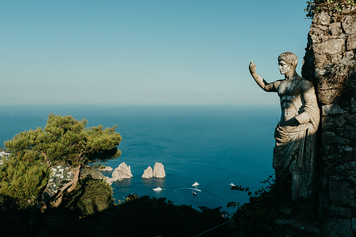 The statue of Augustus and Faraglioni rocks with a body of water and cloudless sky in the background