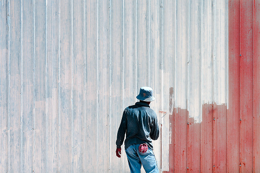 A man wearing a hat painting a light blue wooden wall red