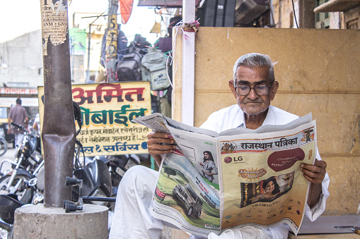 Rajasthan, India – October 15, 2016: An elderly male wearing glasses sitting and reading a newspaper