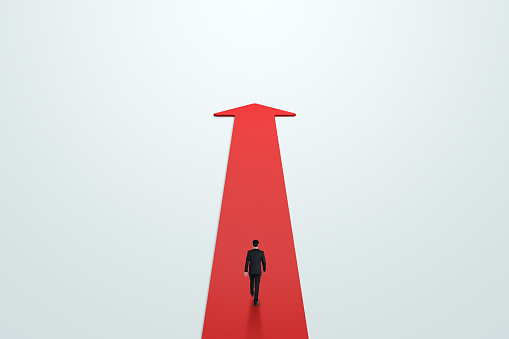 Road to success, achievement and personal development concept with walking on red carpet in form of arrow growing up businessman back view on light background