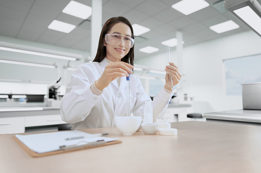 In a modern Laboratory female chief observes test tube research scientist examining substance in a petri dish under microscope.
