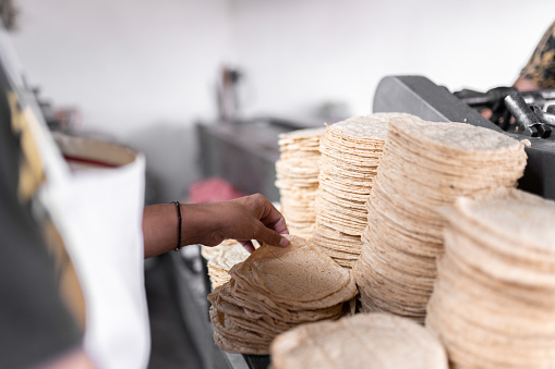 A young man is stacking a lot of fresh baked tortillas of the nixtamall mill. Concept of traditional corn tortillas preparation