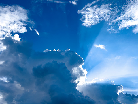 Cloudscape image of shining sun over blue sky. Bright summer skies with dramatic billowing white dreamlike fluffy clouds. Beautiful nature background with large copy space.