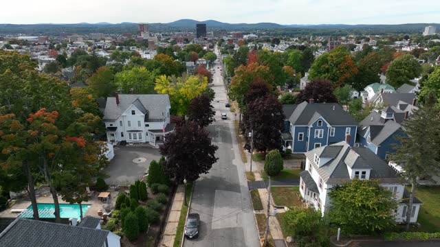 Aerial drone videography of wealthy northeastern neighborhood in fall. Large homes line neighborhood streets where cars travel in the United States