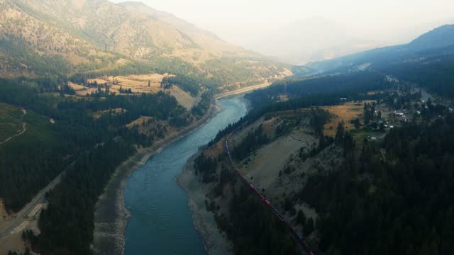 A train moving along the Fraser River in British Columbia. The interior of BC near Lytton and Kamloops, as a train moves through the valley. Sunrise aerial shot of the Fraser River.