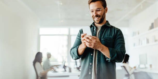 biznesmen czytający wiadomość przez telefon komórkowy w biurze - men holding smiling young adult zdjęcia i obrazy z banku zdjęć