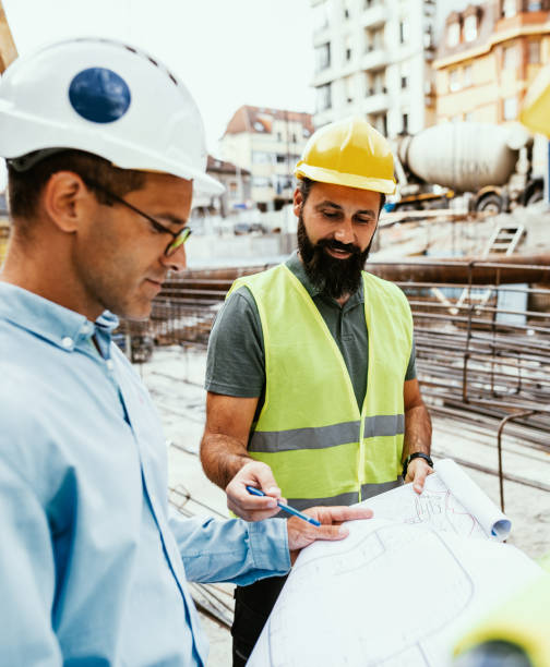 istock Engineers and contractors on construction site, looking at blueprint and talking 1455690546