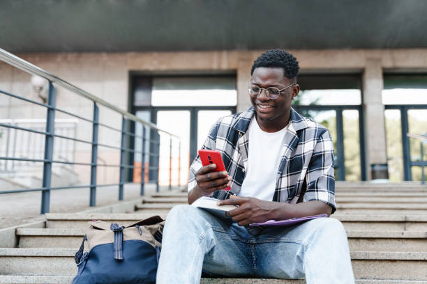 istock African student using mobile phone sitting on University Campus staircase 1455690735