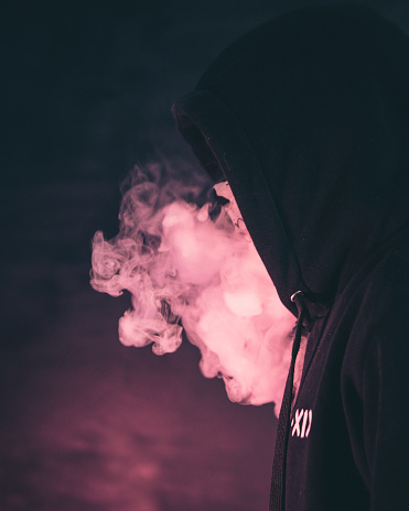 A closeup shot of a man with black hoody on isolated background and smoke