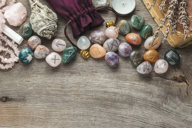 Elder Futhark Rune Stones Set Made of Natural Gemstones, Sage Incense, Candle, Old Book on Wooden Background