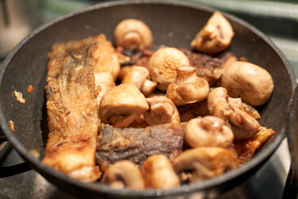 A fried carp fish with mushrooms in the pan.