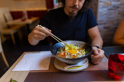 A cut-out shot of one man eating Japanese noodle soup with chopsticks at the restaurant. Asian food concept.