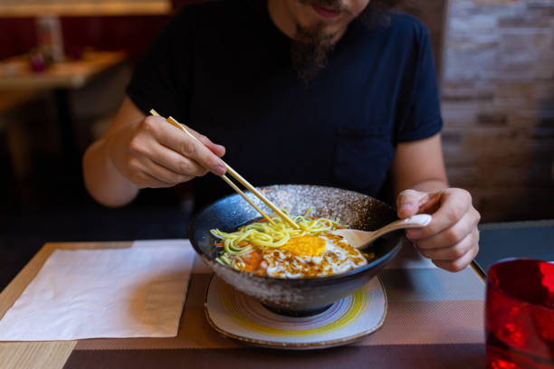 A cut-out shot of one Caucasian man eating Japanese noodle soup with chopsticks at the restaurant. Asian food concept.